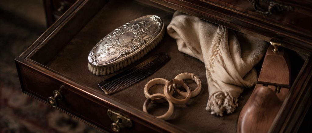 Open mahogany drawer containing a silver clothes brush, horn comb, cedar rings, folded cream cloth and a wooden shoe tree